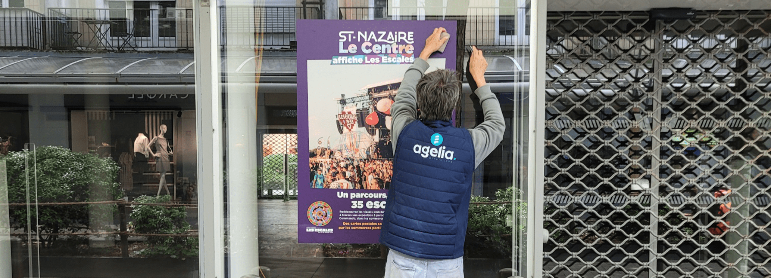 un poseur avec une doudoune agelia colle une affiche sur une vitre